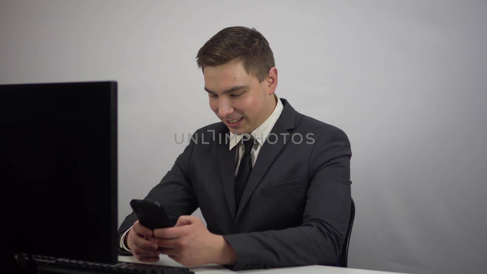 Businessman chatting in smartphone while working. A young man in a suit sits in an office with a smartphone in his hands. 4k