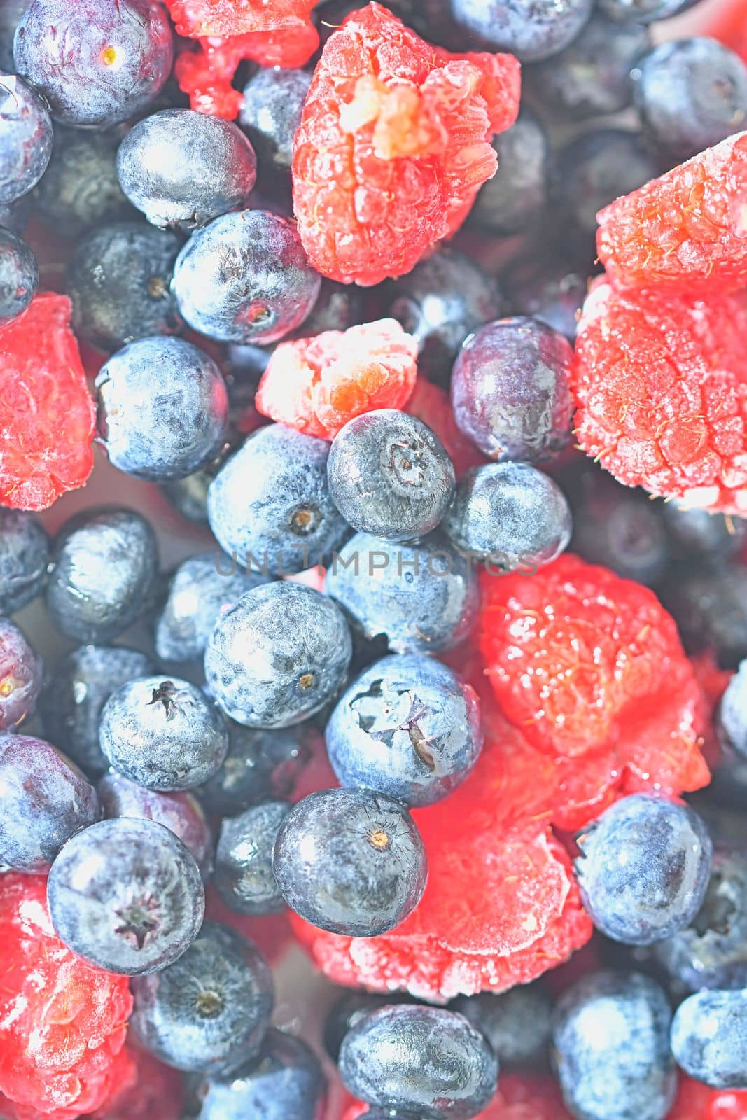 Frozen fresh blueberries and raspberries, close-up. Close-up view of bilberries and raspberries. Texture of frozen berries. Flat design, top view. Vertical image by roman_nerud