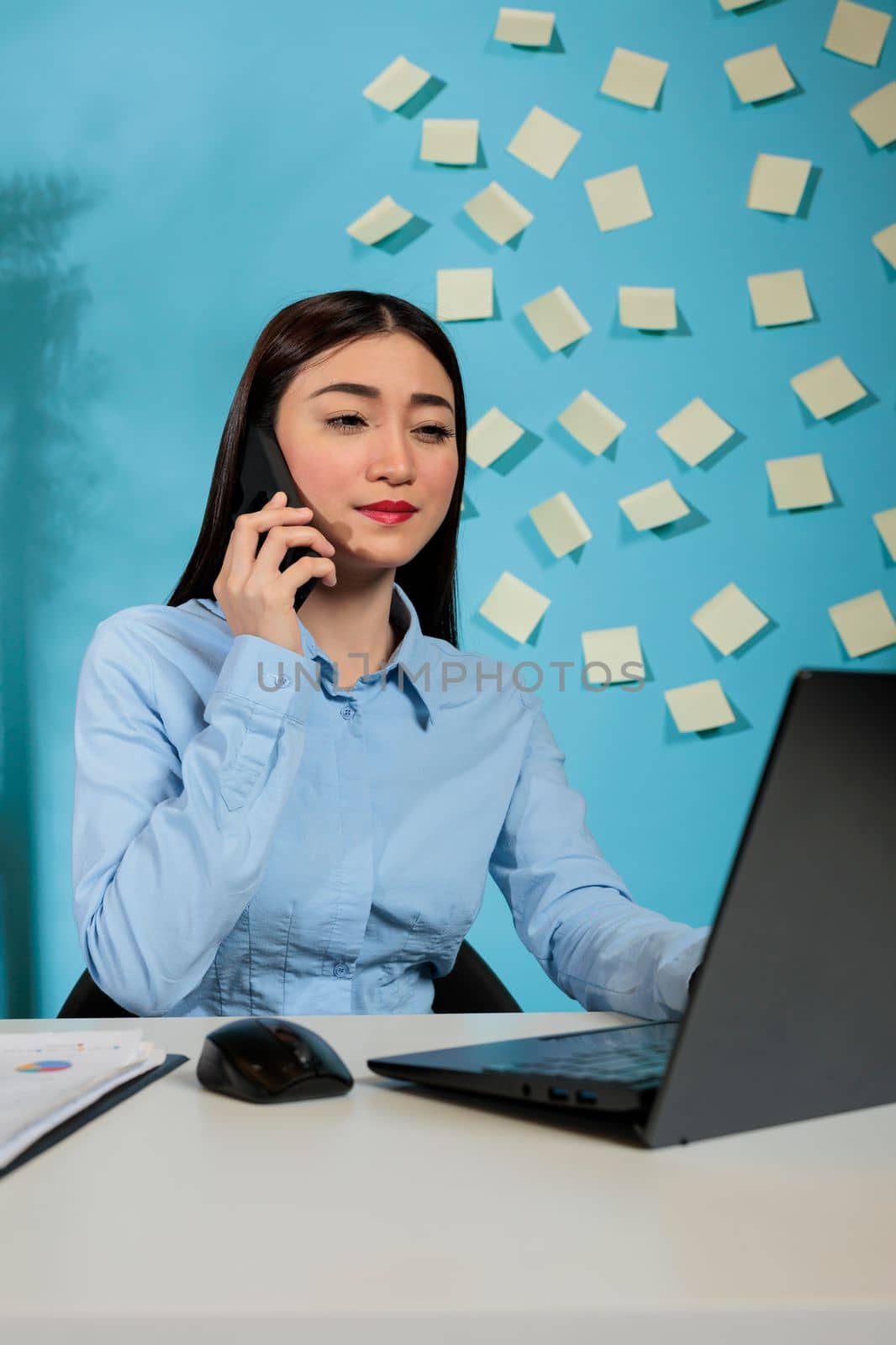 Professional asian woman in contemporary office talking on phone by DCStudio