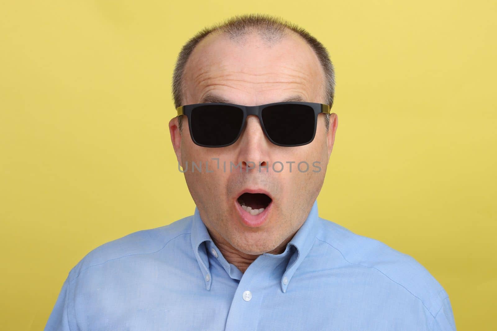 Handsome man in a blue shirt and black glasses in after 40 years on a yellow background.