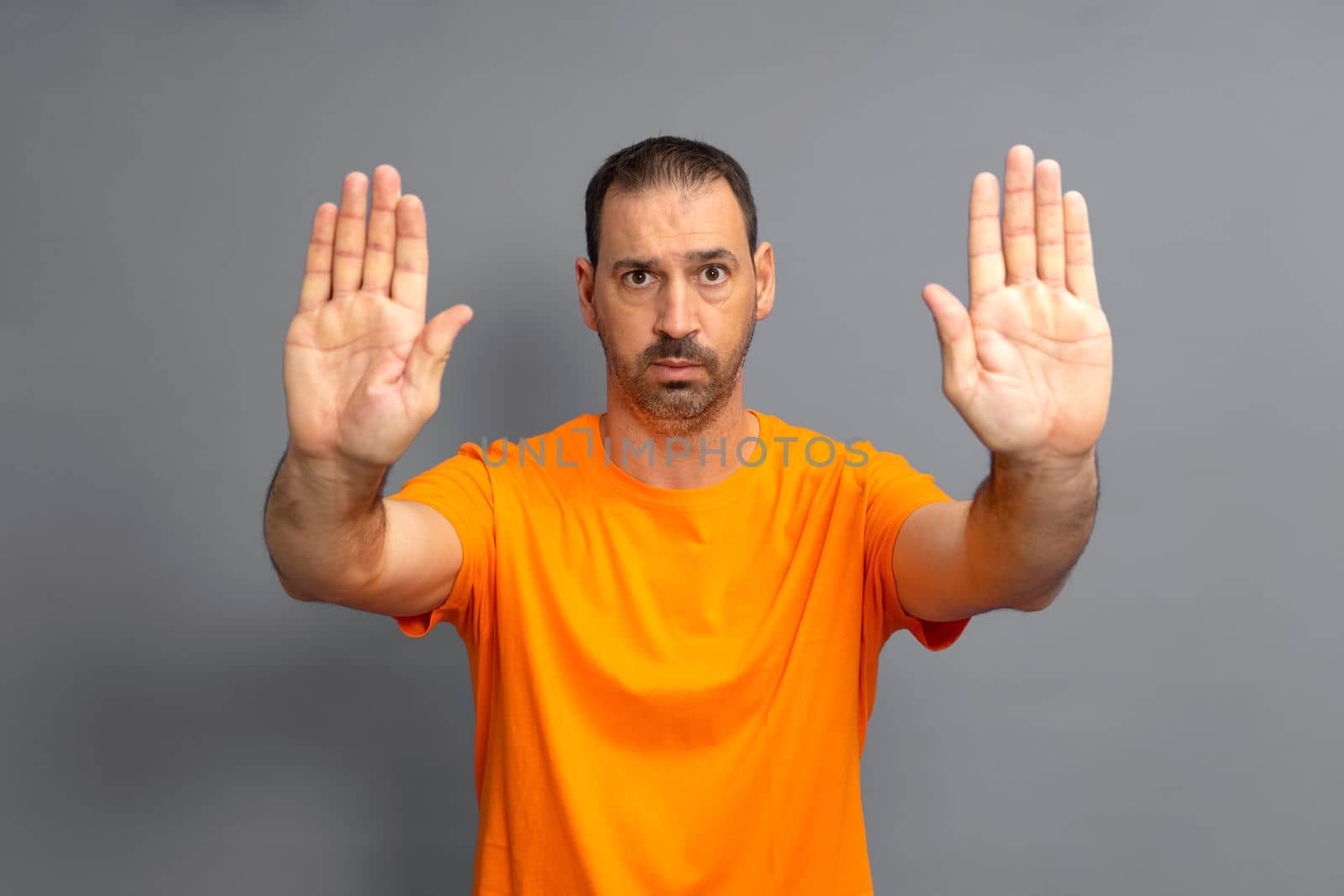 Bearded hispanic man wearing casual orange t-shirt turning away hands showing rejection and denial with scared and disgusting expression. Stop and prohibited.