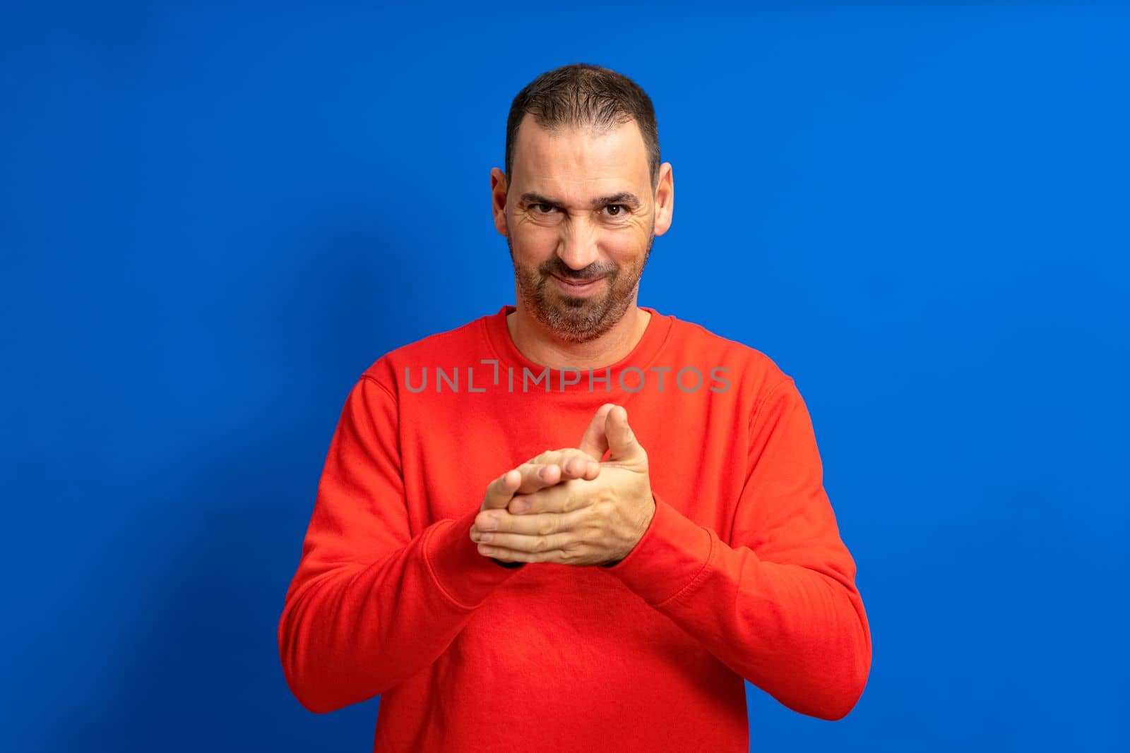 Latino handsome man feeling proud, mischievous and arrogant while hatching an evil plan or thinking up a trick. Isolated on blue background