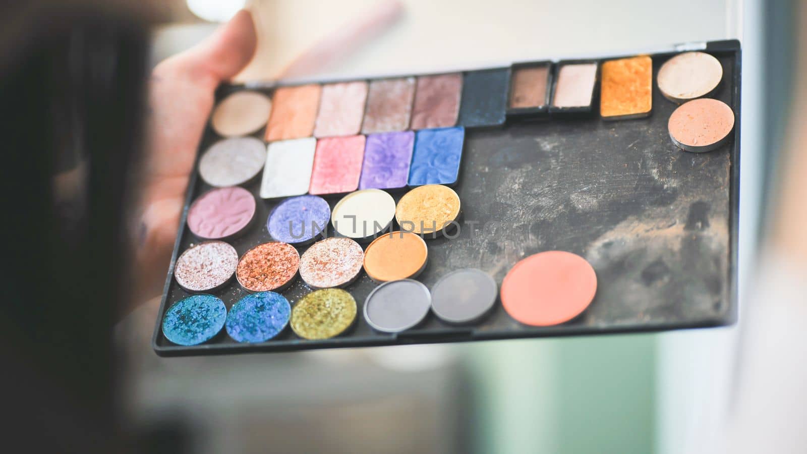 The makeup artist is holding a palette of shadows