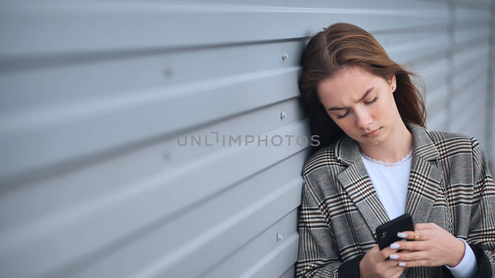 A disgruntled girl stares into a smartphone against a striped wall