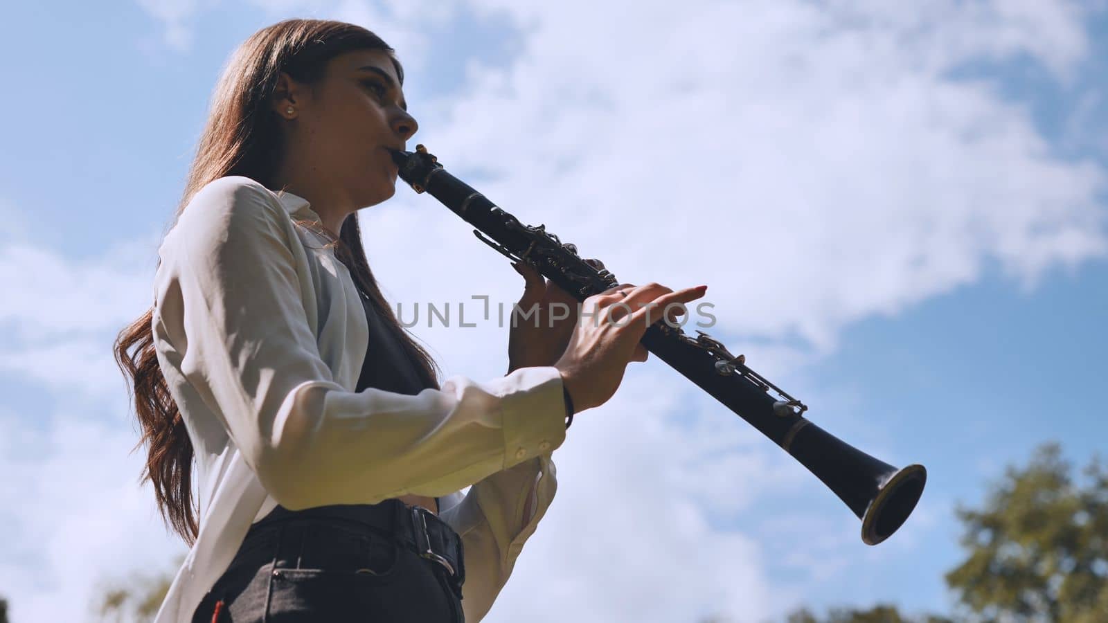 Girl plays clarinet against sky