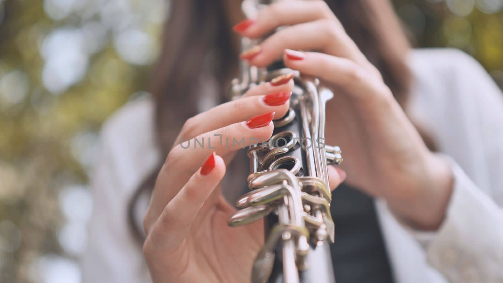 A girl plays the clarinet in the summer in the park. Close-up of her hands