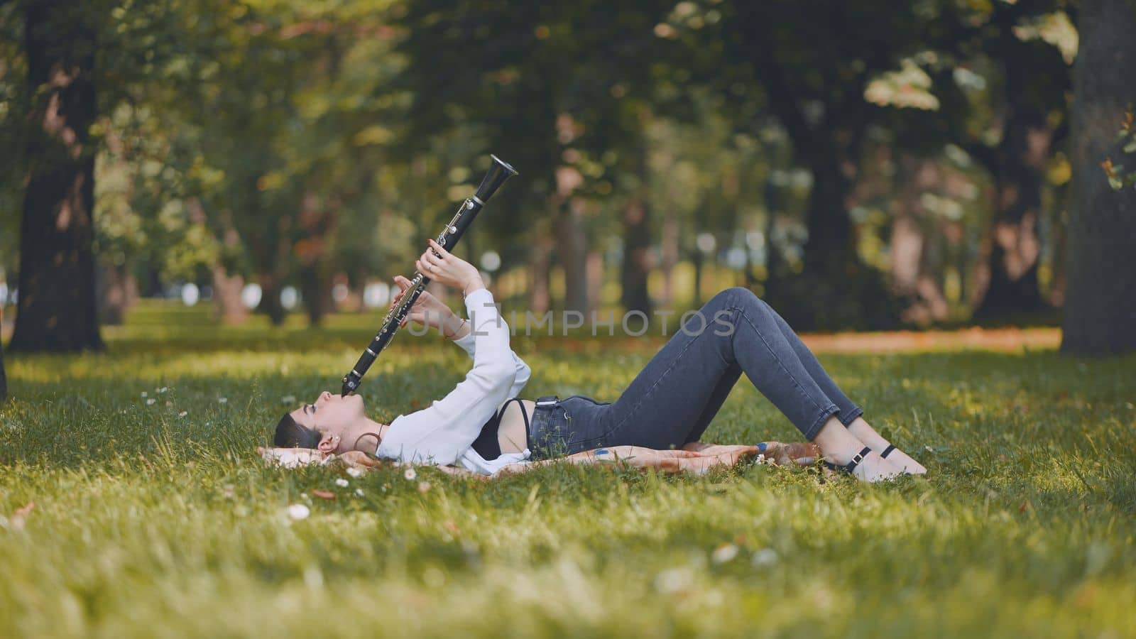 A girl plays the clarinet while lying on the grass in the park