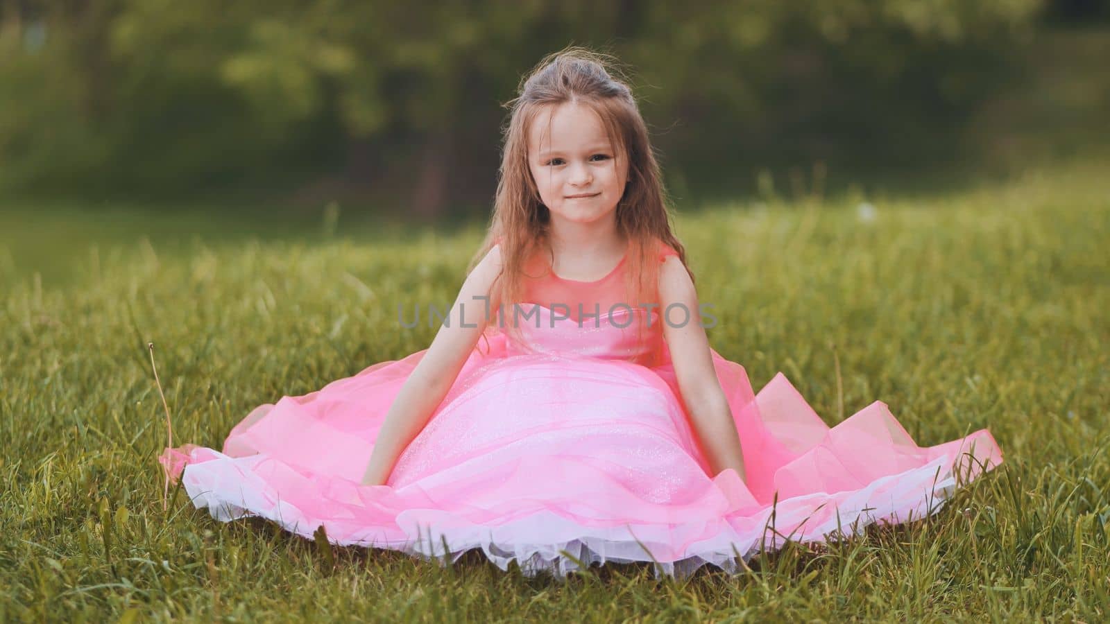 A little girl is sitting in a pink dress in the park