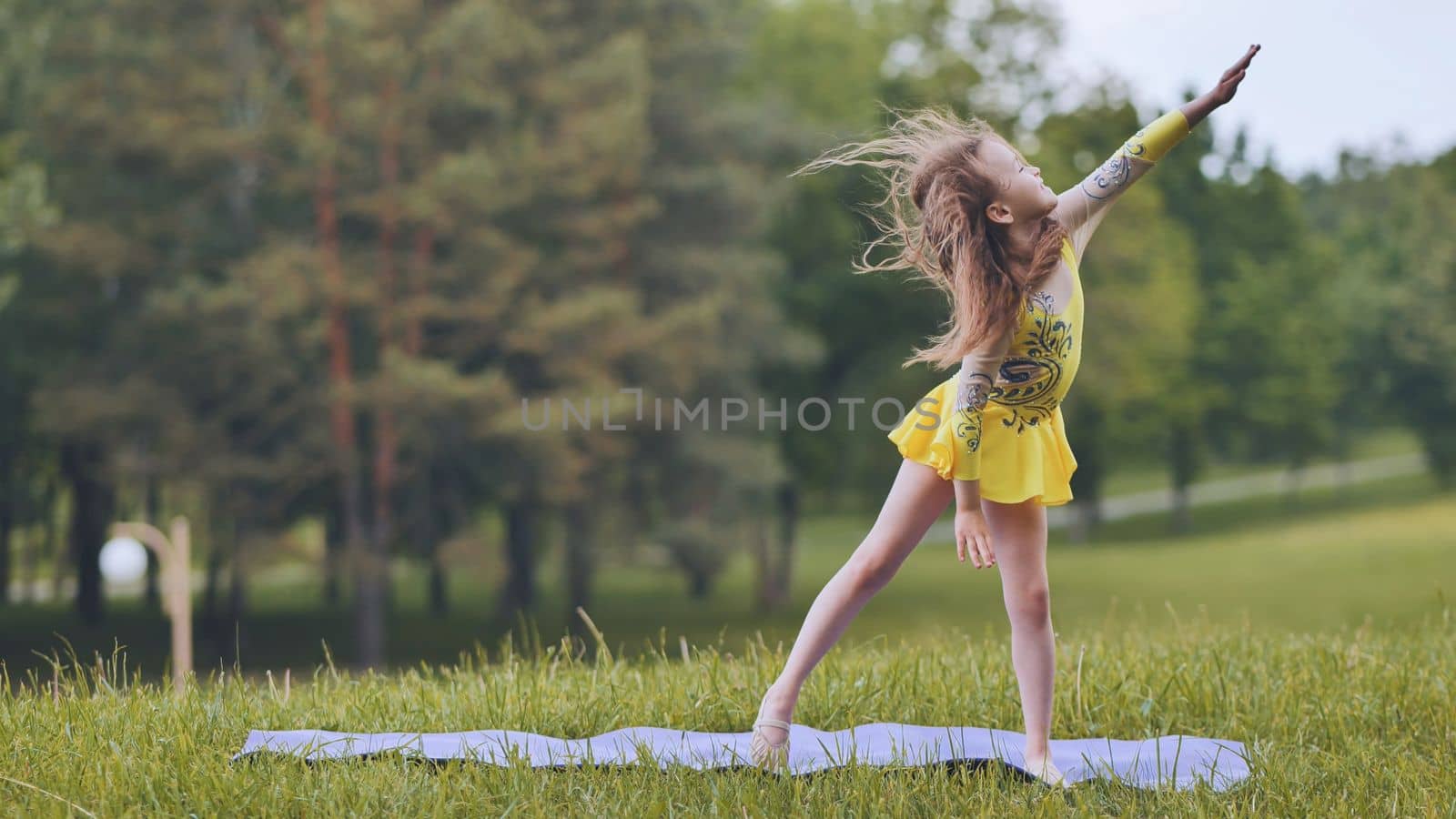 A little girl performs the elements of rhythmic gymnastics in the park