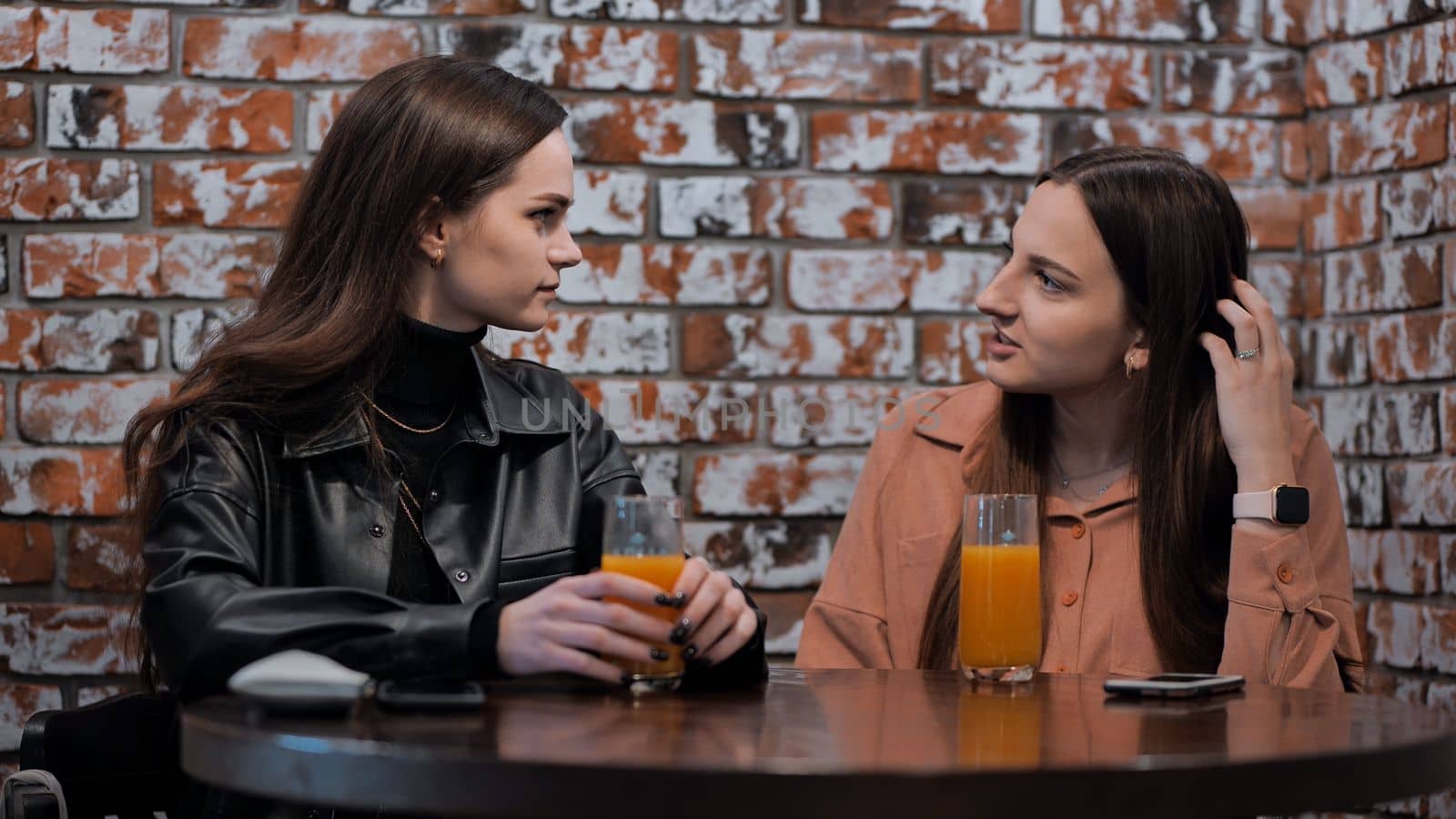 Two brown-haired girls talk in a cafe over glasses of juice. by DovidPro