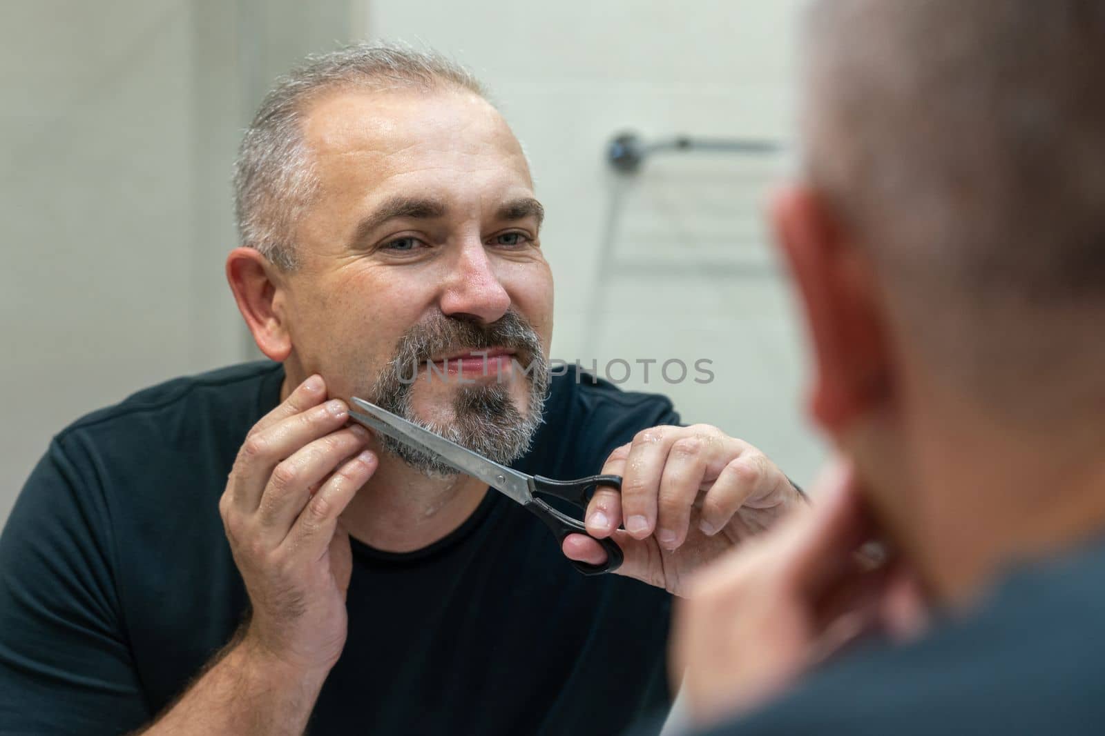 Portrait of Middle-aged handsome man cutting his beard and mooustache with scissors by Mariakray