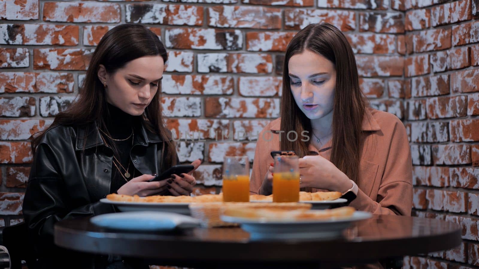Two beautiful girls are sitting in a cafe and talking with phones