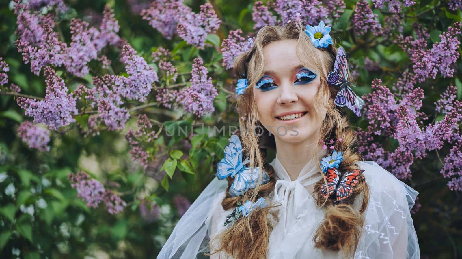 A young girl poses in lilac with a beautiful hairstyle of flowers and butterflies
