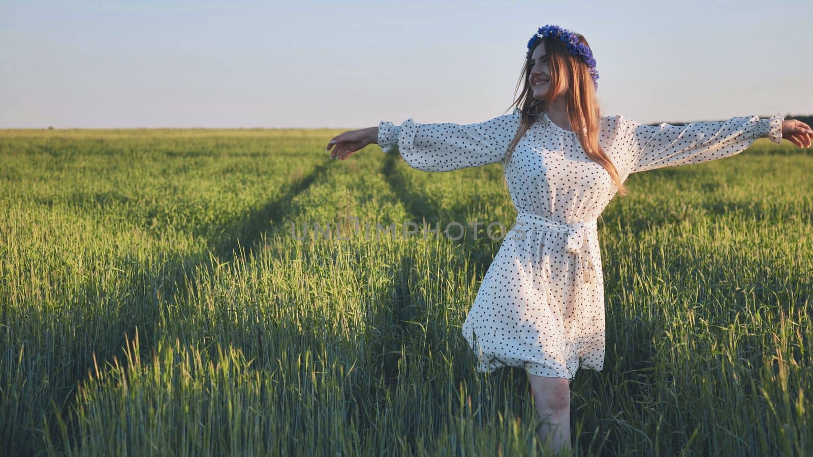 A young Ukrainian girl walks through a young wheat field