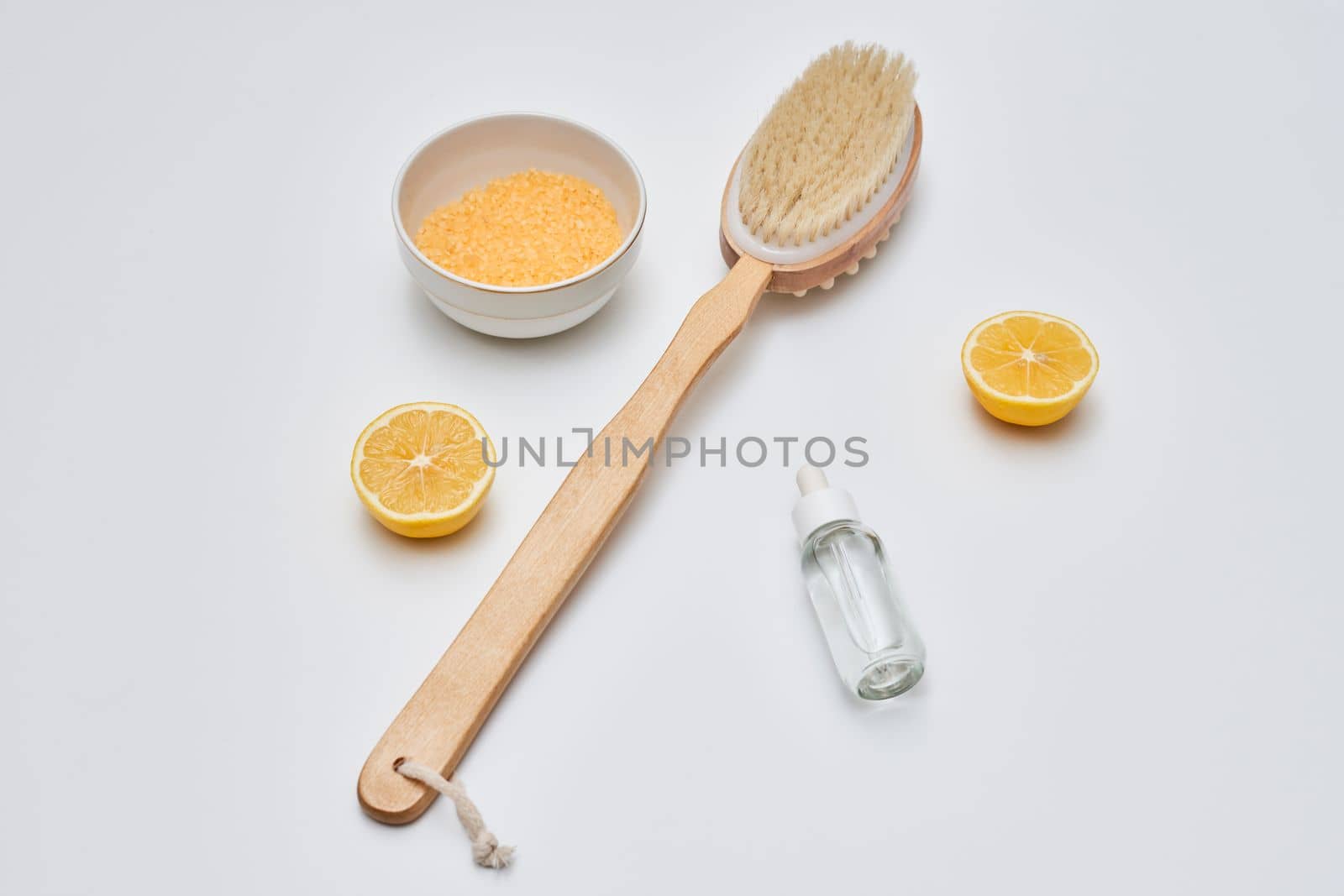 a wooden brush and some lemons on a white surface with a small bottle of essential oil in the background
