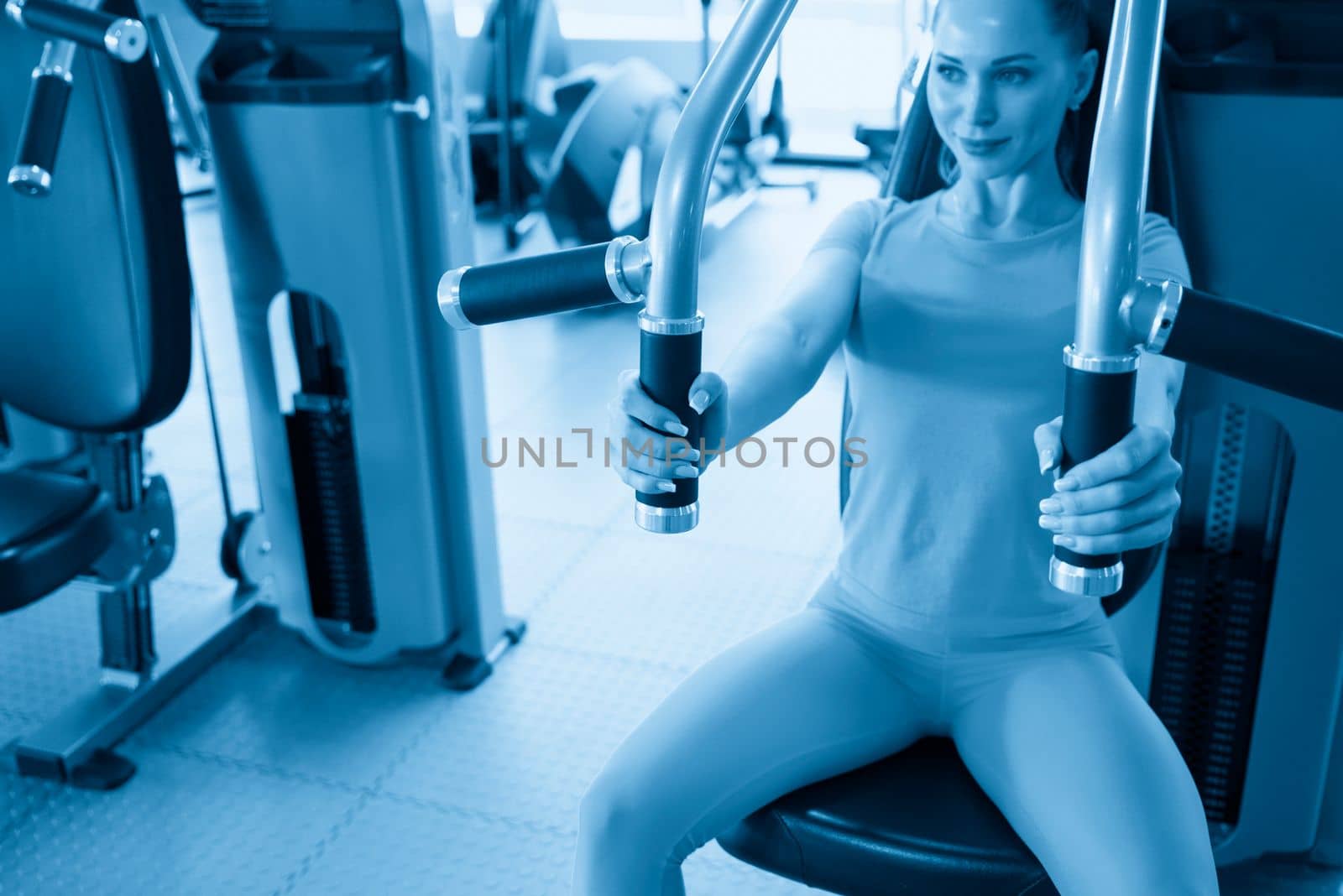 Torso portrait of Cheerful young adult caucasian woman working out on exercise machine inside gym by Mariakray