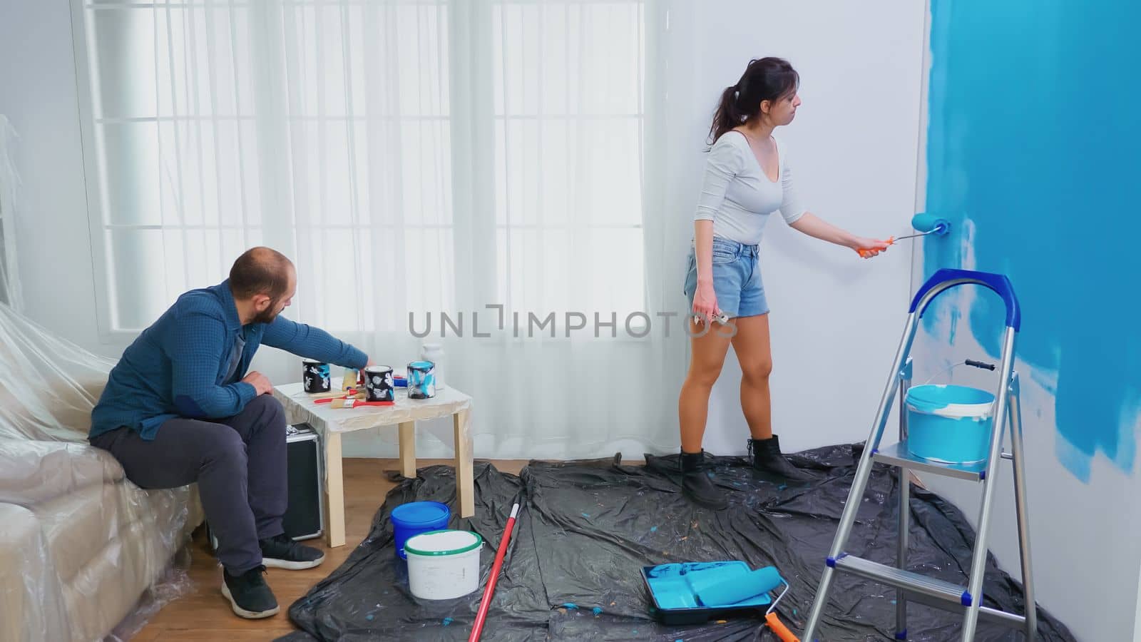 Wife painting wall with roller brush by DCStudio