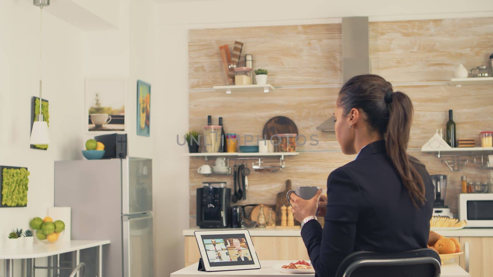 Business woman during a video call with friends while eating breakfast before leaving to the office. Using modern online internet web technology to chat via webcam videoconference app with relatives, family, friends and coworkers