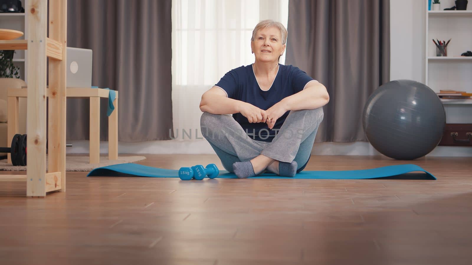 Portrait of senior woman sitting on yoga mat. Active healthy lifestyle sporty old person training workout home wellness and indoor exercising