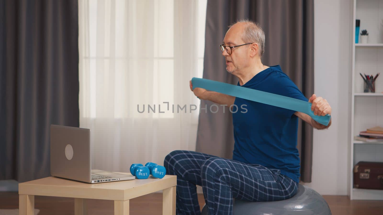 Senior man with vitality doing fitness exercise with resistance band watching online program. Old person pensioner healthy training healthcare sport at home, exercising fitness activity at elderly age