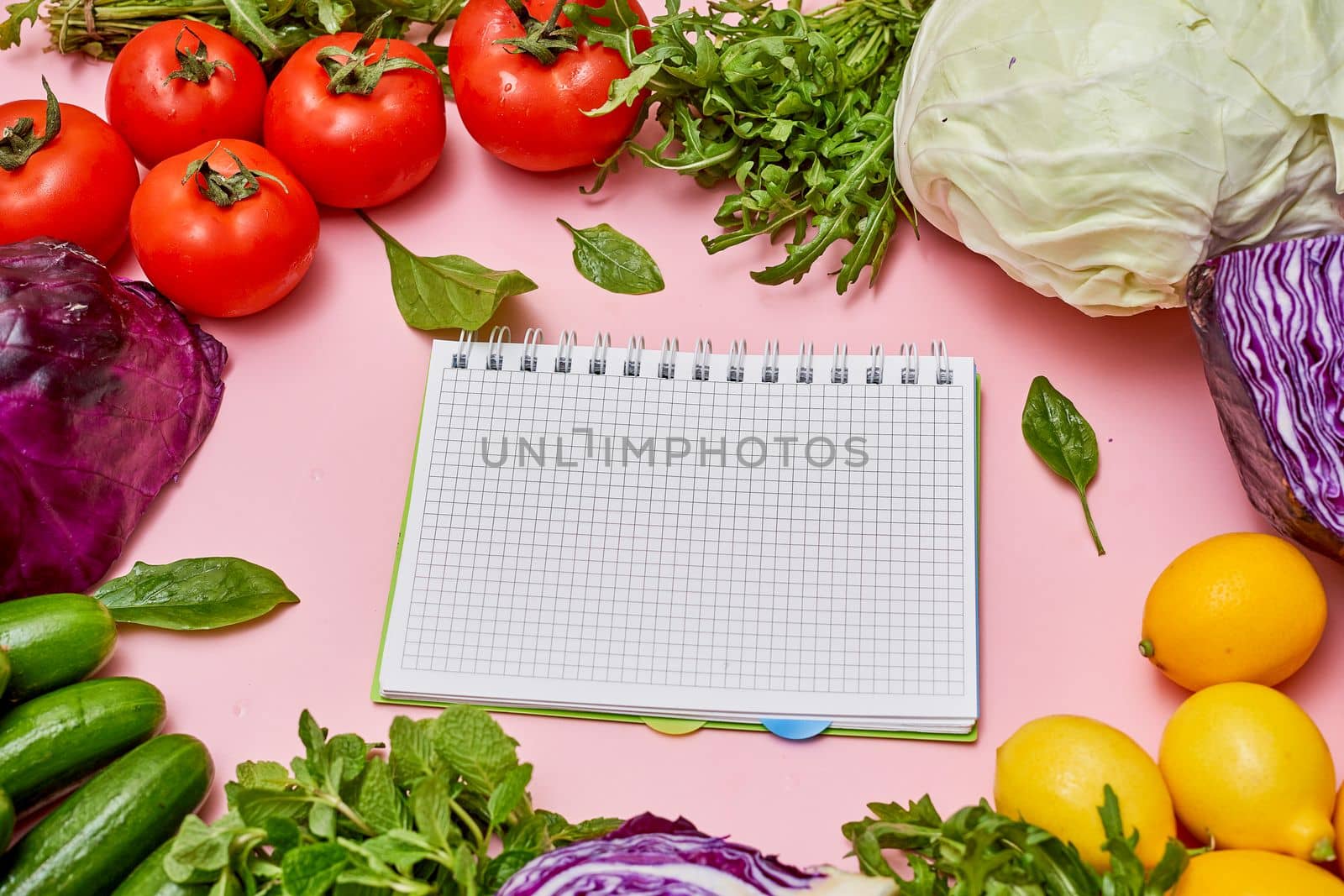various vegetables and fruits on a pink background with a notepad in the middle that has been used for writing