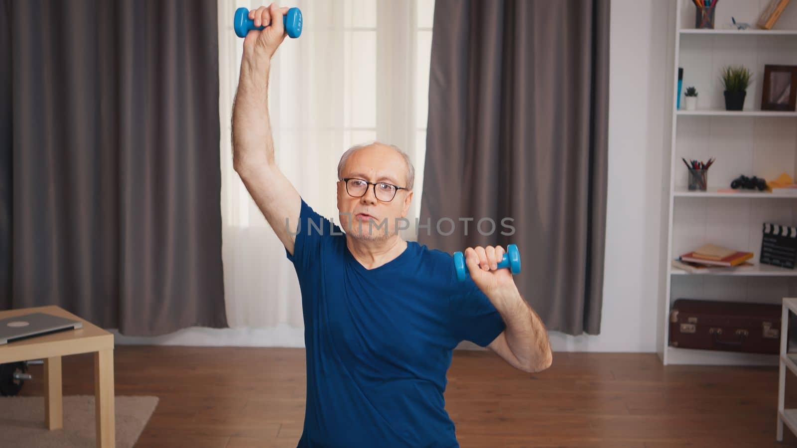 Senior man doing sports in living room using dumbbells. Old person pensioner healthy training healthcare sport at home, exercising fitness activity at elderly age