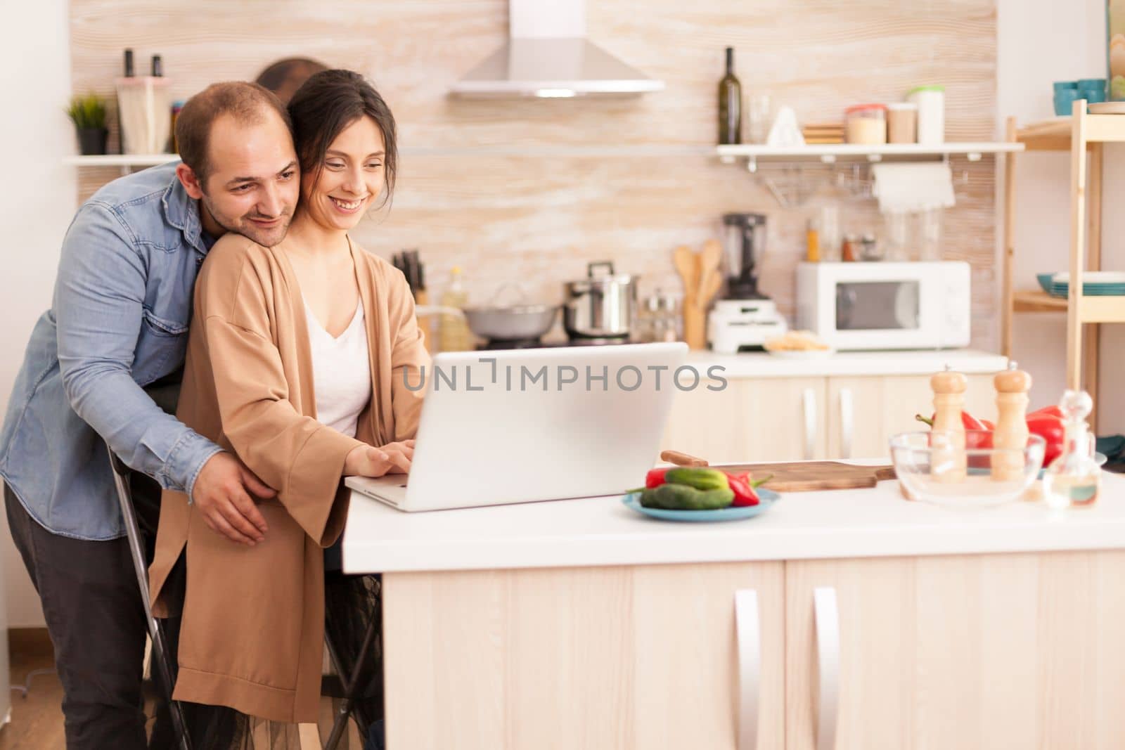 Cheerful couple using laptop in kitchen reading online recipe for breakfast. Happy loving cheerful romantic in love couple at home using modern wifi wireless internet technology