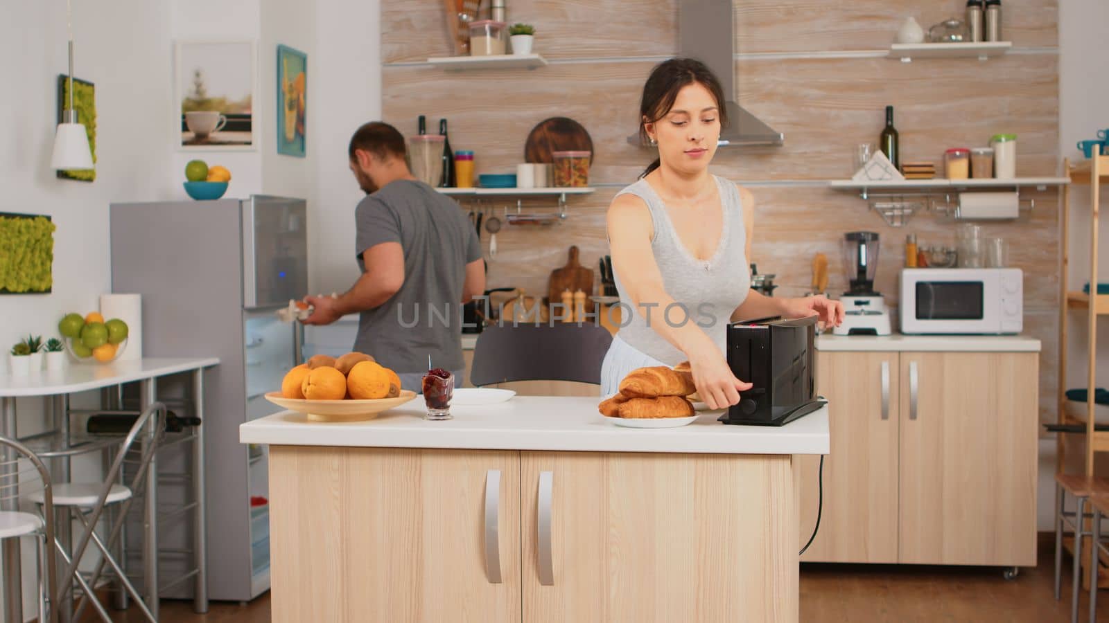 Housewife in pajamas preparing breakfast making roasted bread on electric toaster. Young couple in the morning preparing meal together with affection and love