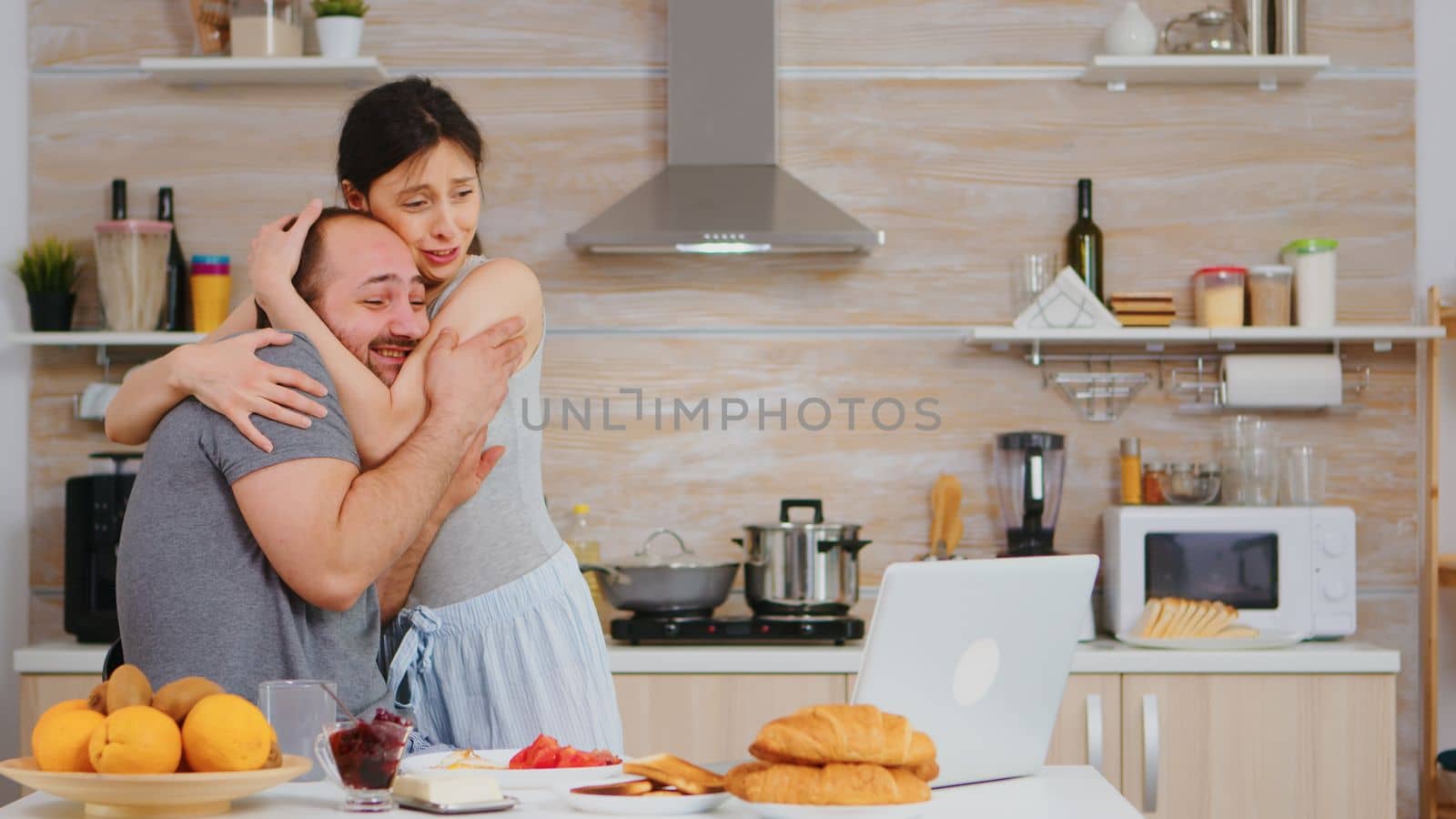 Young freelancer reads good news while having breakfast and working on laptop in kitchen. Successful overjoyed euphoric entrepreneur at home in the morning, winner and business triumph