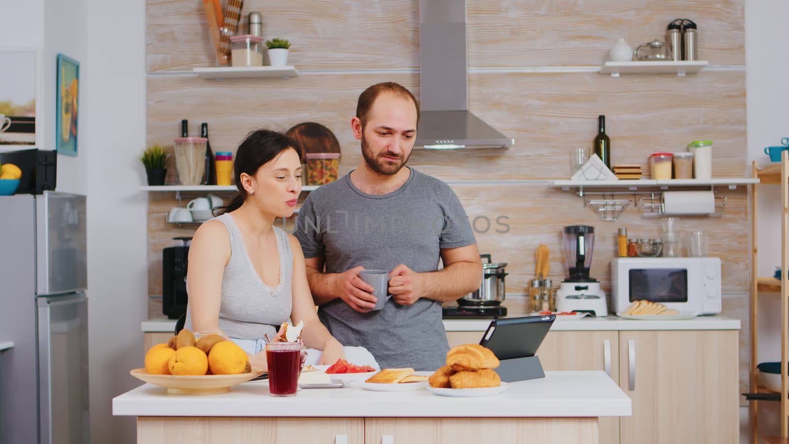 Couple waving during video call while eating delicious breakfast in kitchen. Videoconference in the morning, using online web internet technology, talking and communicating with relatives