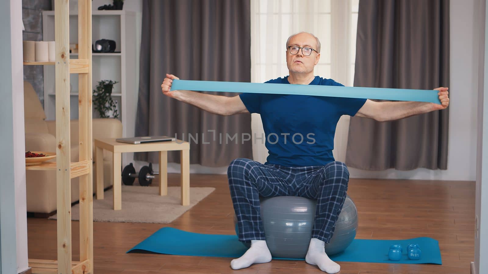 Senior man in sports wear exercising with resistance band. Old person pensioner healthy training healthcare sport at home, exercising fitness activity at elderly age