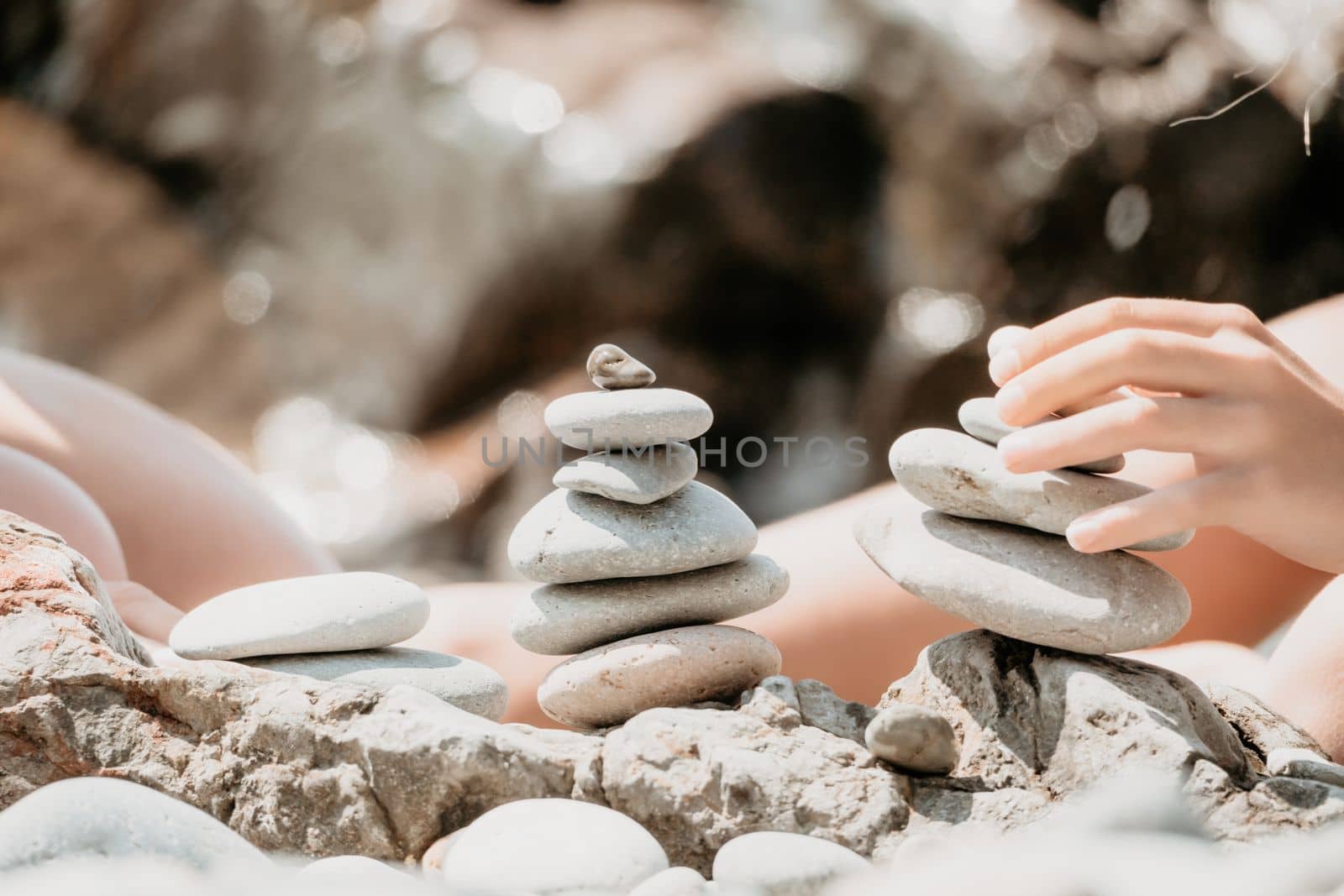 Woman with daughter bilds stones pyramid on seashore on a sunny day on the blue sea background. Happy family holidays. Pebble beach, calm sea. Concept of happy vacation on the sea, meditation, spa by panophotograph