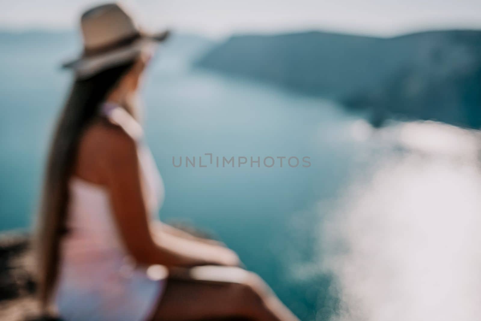 Digital nomad, woman in the hat, a business woman with a laptop sits on the rocks by the sea during sunset, makes a business transaction online from a distance. Freelance, remote work on vacation. by panophotograph