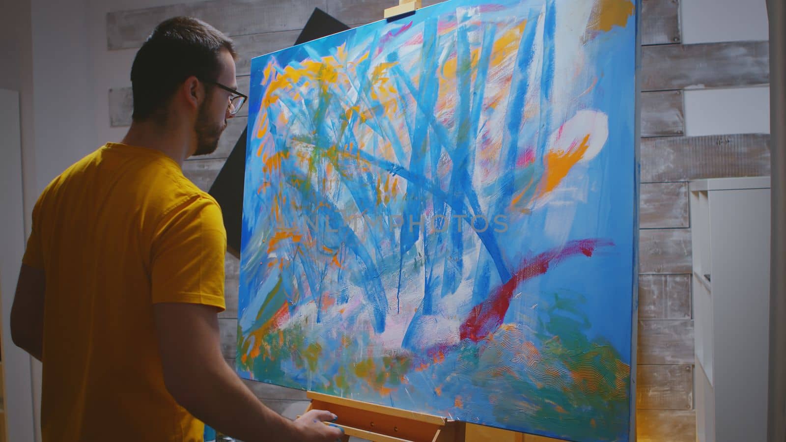 Artist paints on large canvas with fingertips in art studio.