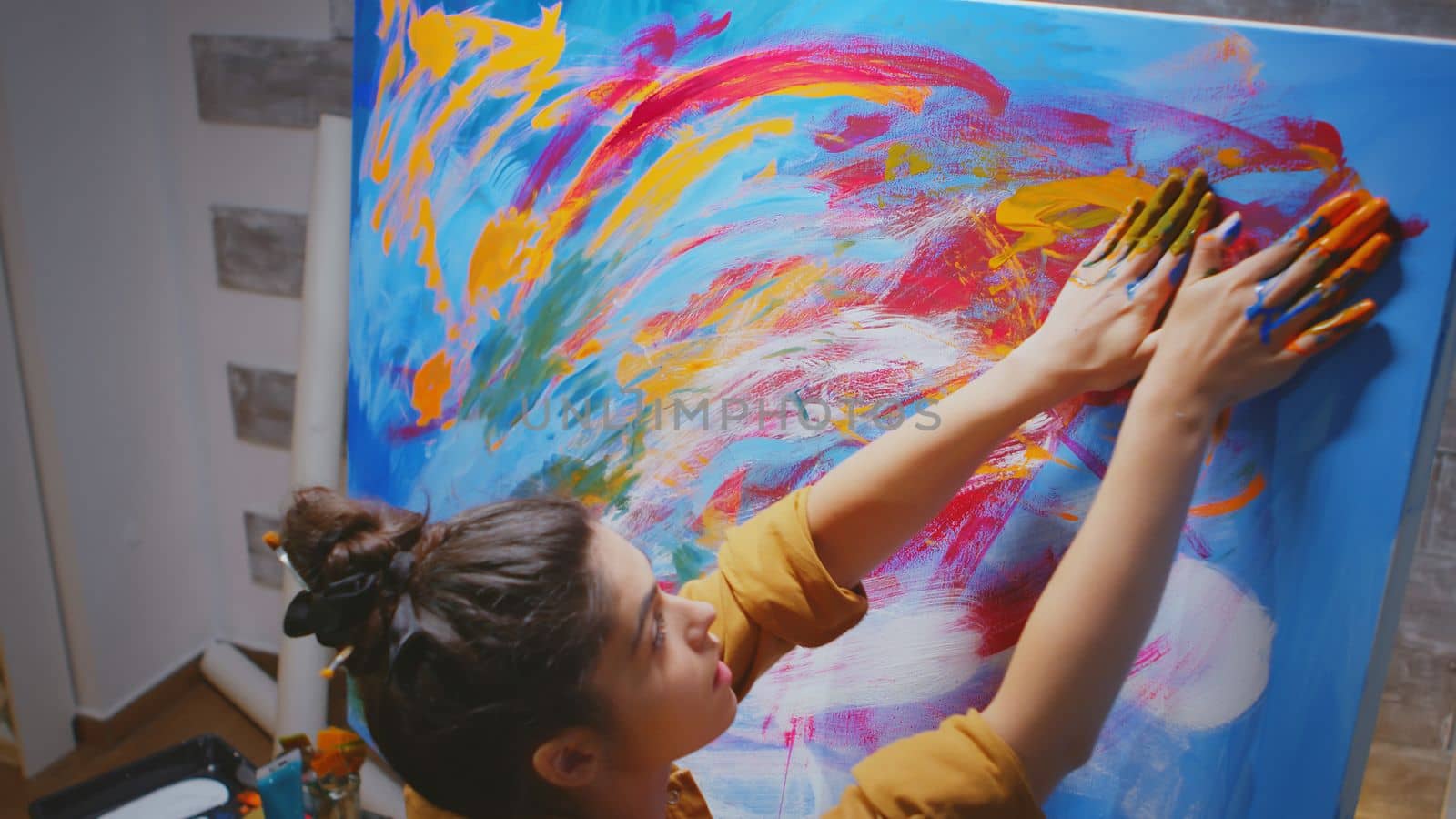 Woman using hand fingers while painting on large canvas in art studio.