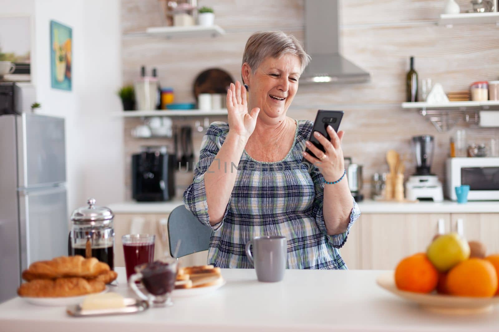 Senior woman saying hello while having video call with family using smartphone by DCStudio