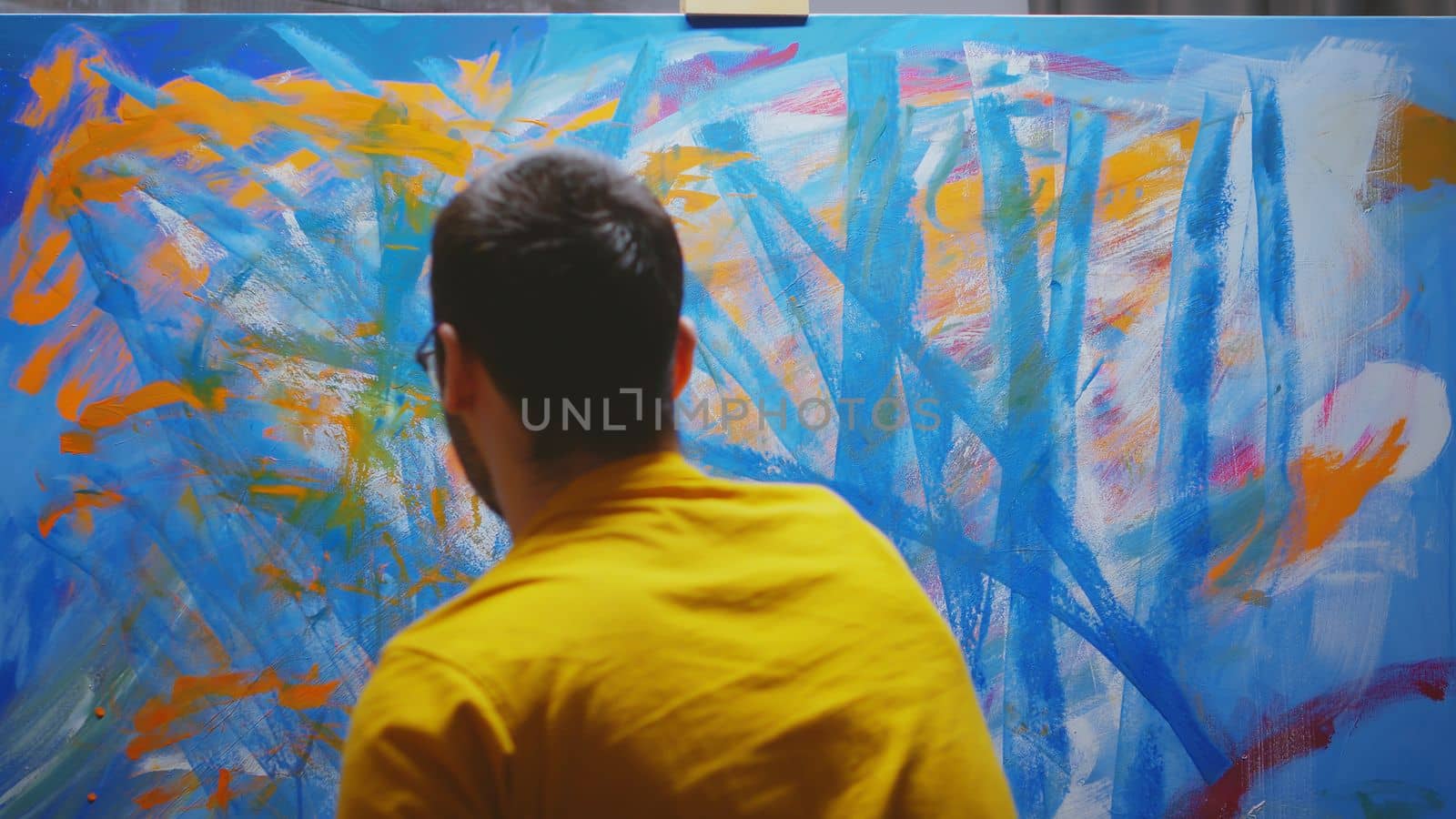 Male artist painting in studio with hands on canvas.