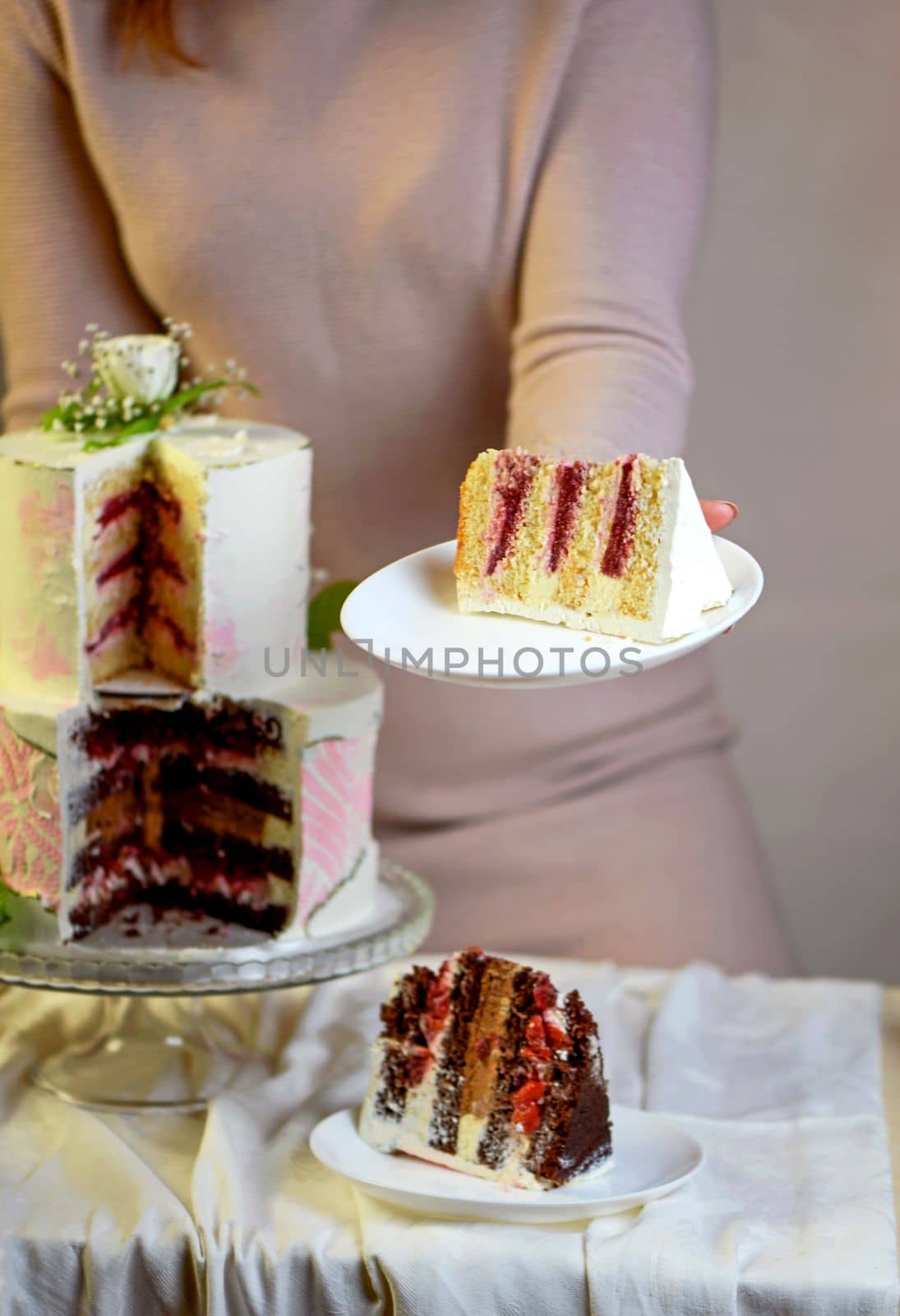 Confectioner prepares, cuts and serves a festive wedding two-tiered cake decorated with fresh flowers on a gray background by aprilphoto