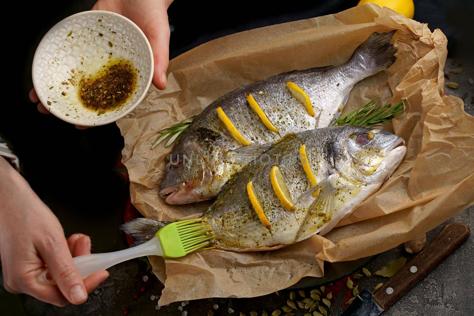 Fresh raw dorado or sea bream with lemon, herbs, olive oil and spices on black background, top view with copy space