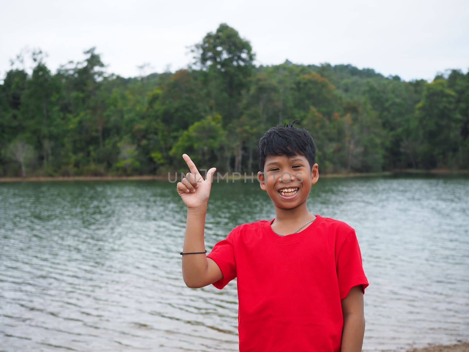The boy smiled and pointed his hand to his side. On the background is a reservoir. by Unimages2527