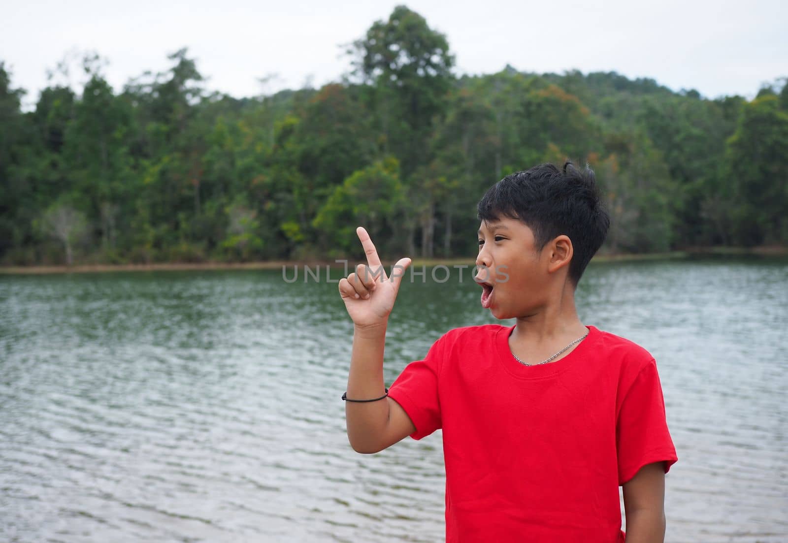 The boy smiled and pointed his hand to his side. On the background is a reservoir.