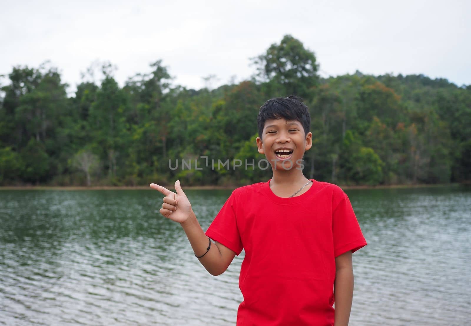 The boy smiled and pointed his hand to his side. On the background is a reservoir.