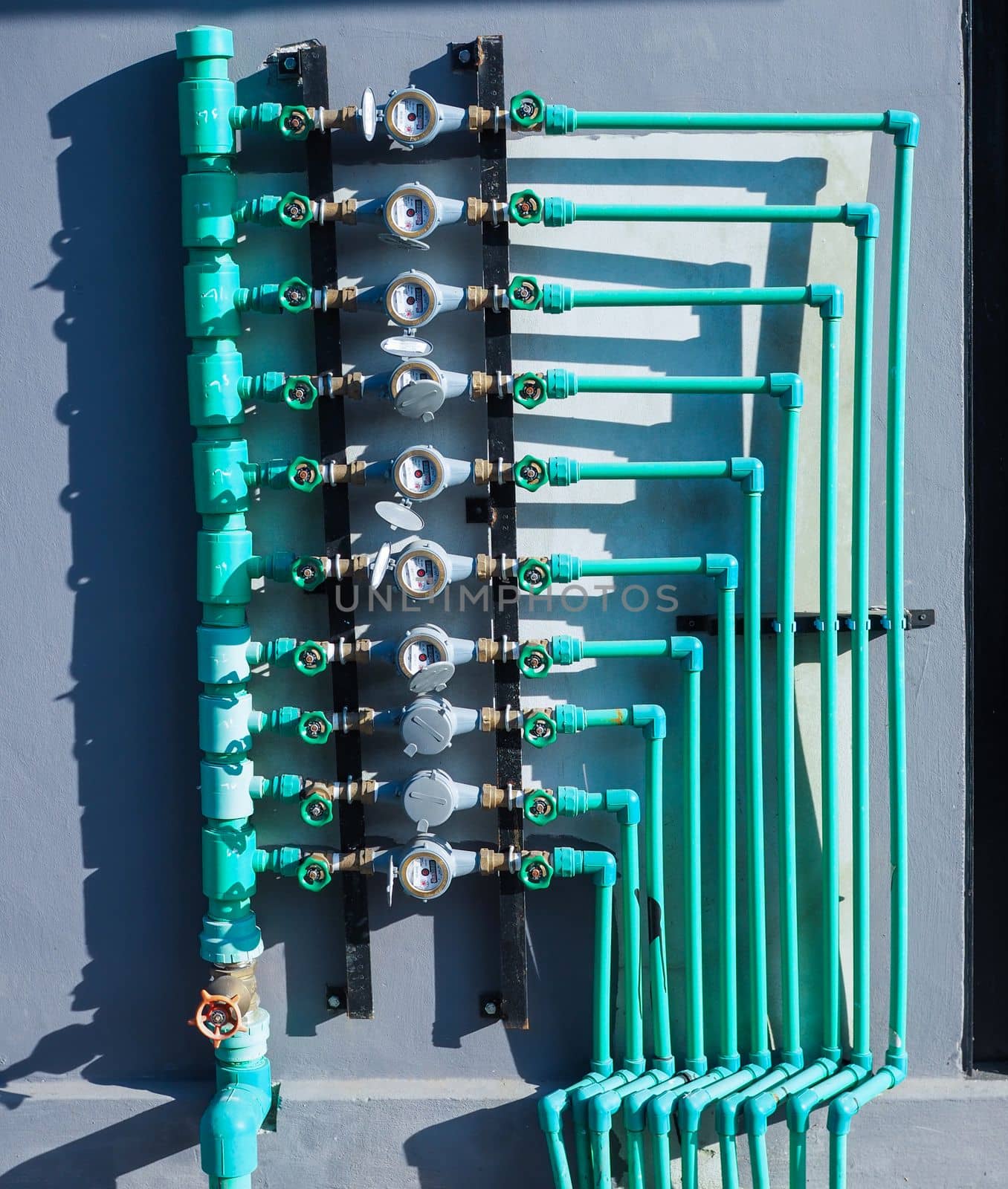Water meter panels, water valves, and green water pipes arranged on the wall of the building