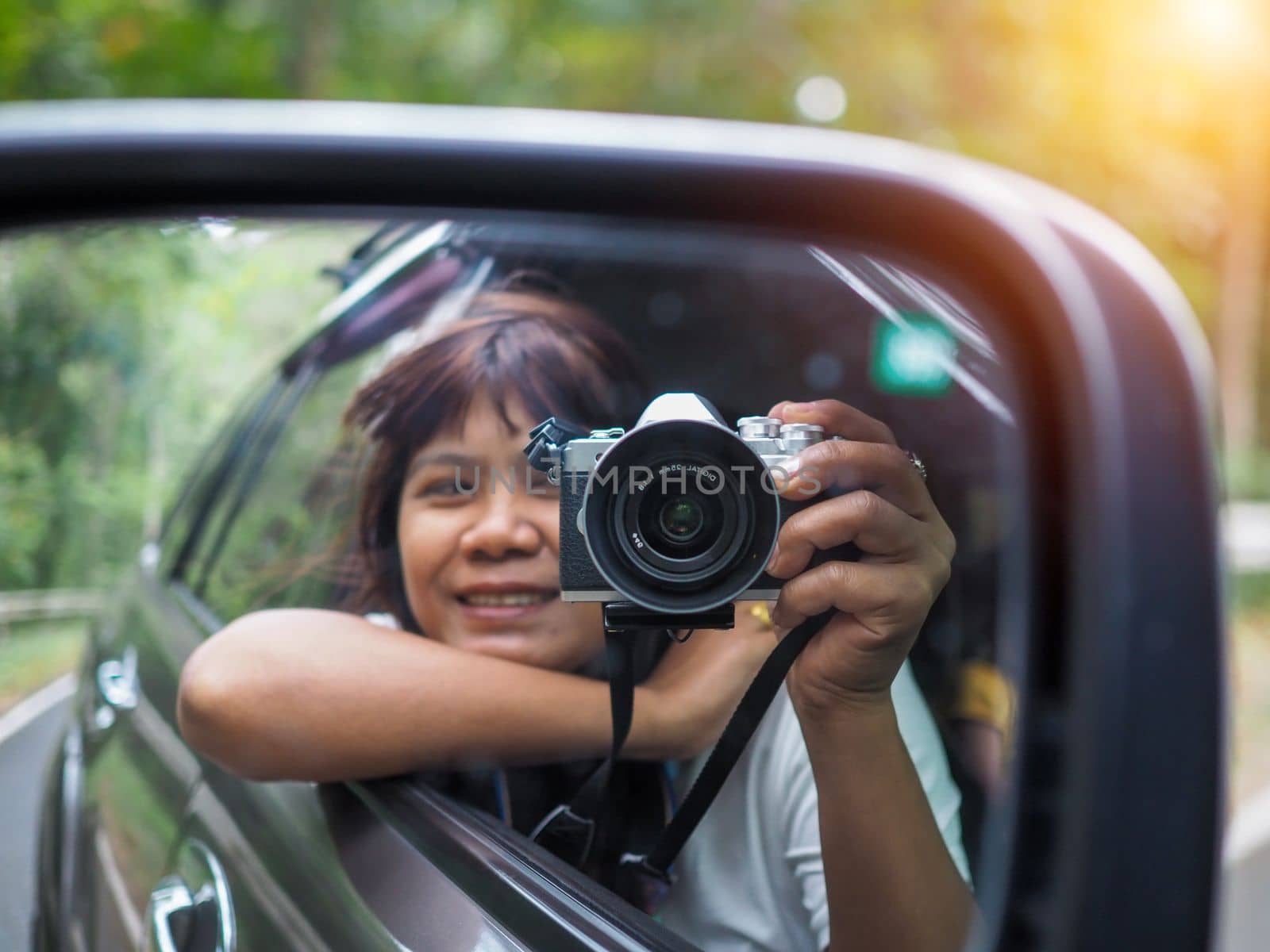 A woman holds a digital camera and takes a picture of herself smiling reflected in the car mirror.