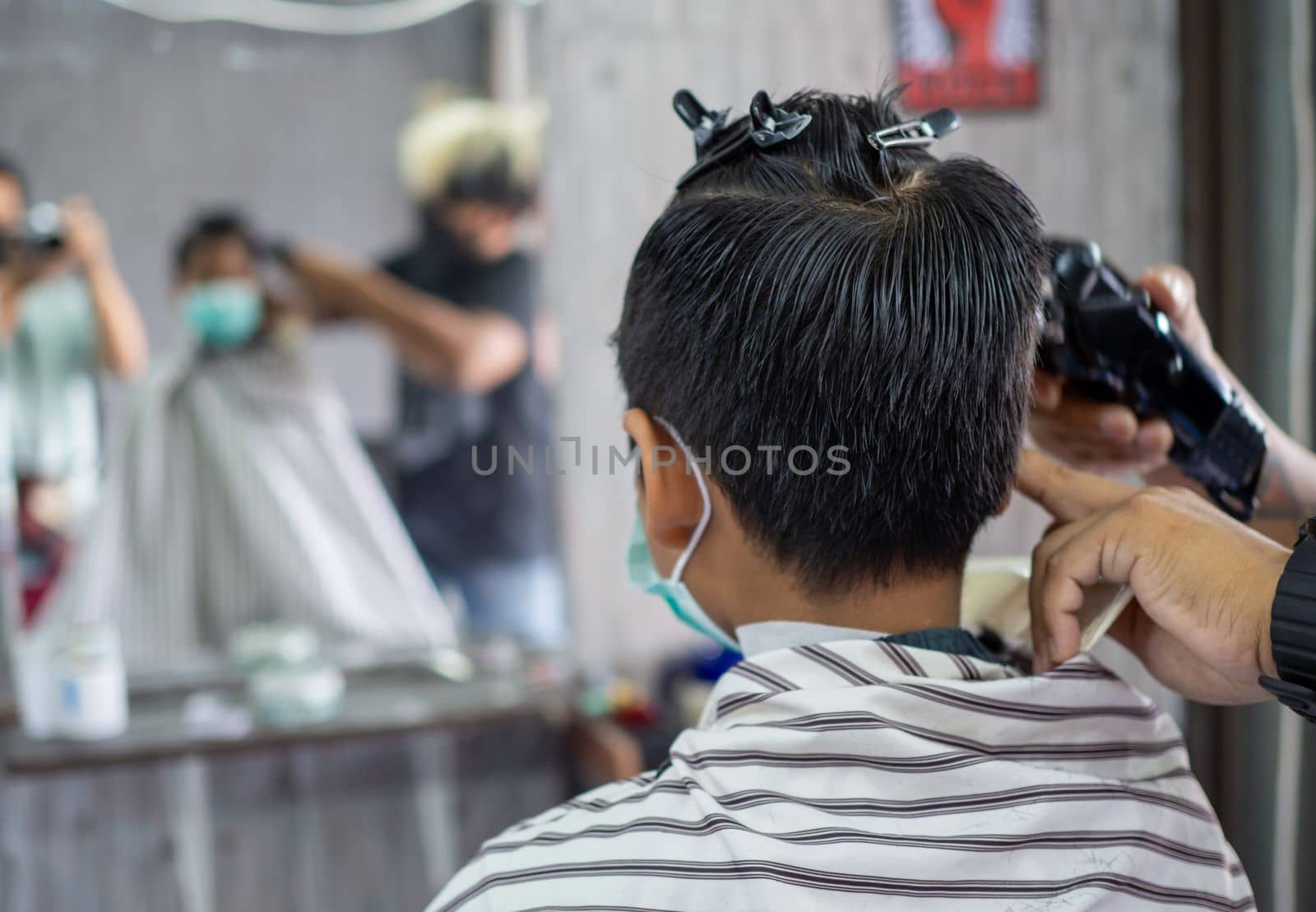 Teenage boy in a face protective mask is getting a haircut from a barbershop. Fashionable elongated haircuts for boys. Beauty salon in quarantine coronavirus covid-1 by Unimages2527