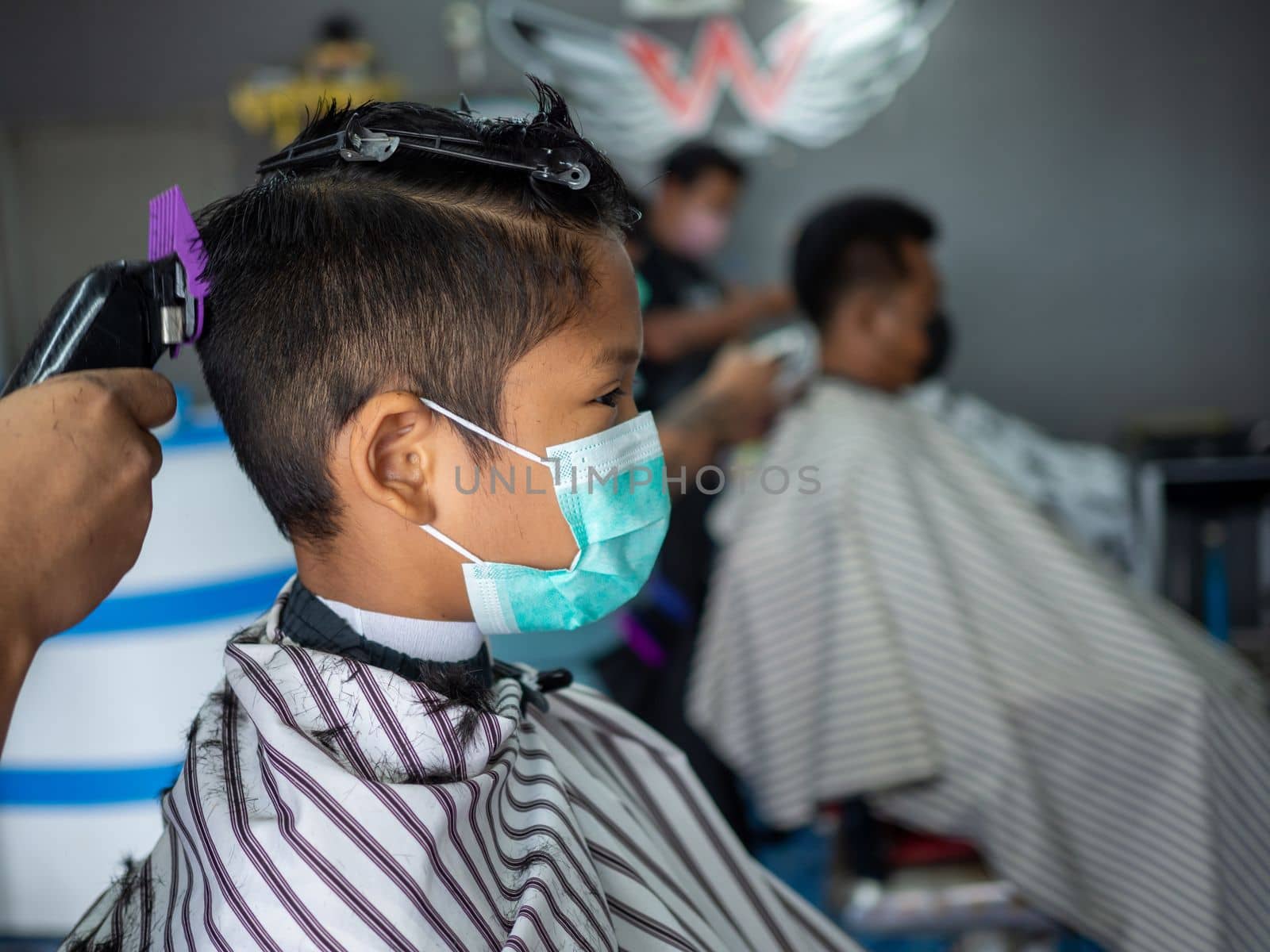 Teenage boy in a face protective mask is getting a haircut from a barbershop. Fashionable elongated haircuts for boys. Beauty salon in quarantine coronavirus covid-1