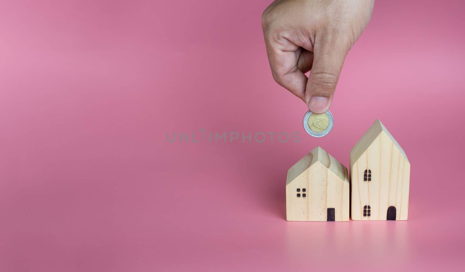 A human hand put a coin in the model house. Ideas for saving money to buy a new home and loans for planning future real estate investments.