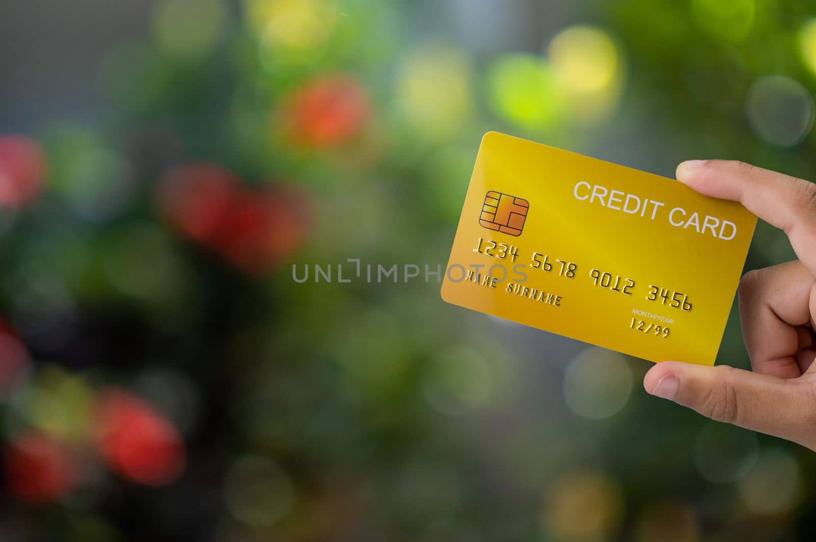 Hand holding credit card on nature bokeh background. Shopping concept. Cashless spending concept.