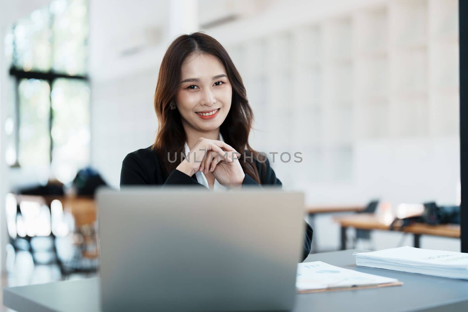 Portrait of a woman business owner showing a happy smiling face as he has successfully invested her business using computers and financial budget documents at work by Manastrong