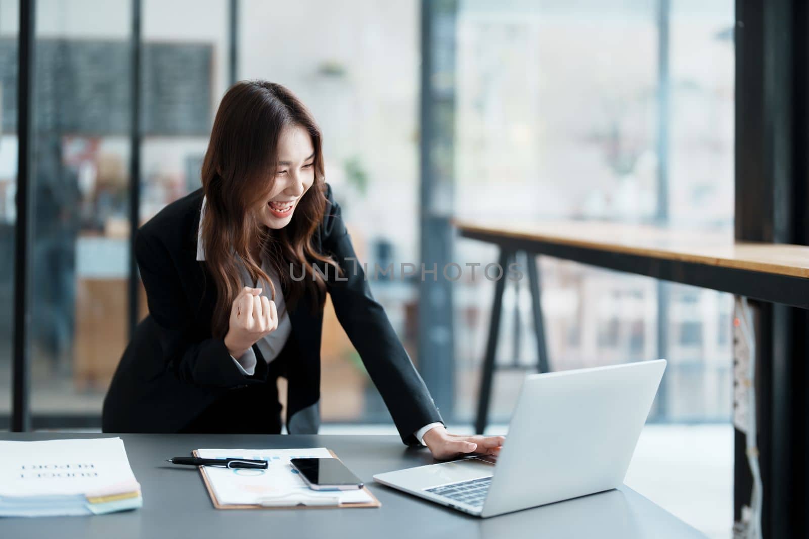 Portrait of a woman business owner showing a happy smiling face as he has successfully invested her business using computers and financial budget documents at work by Manastrong